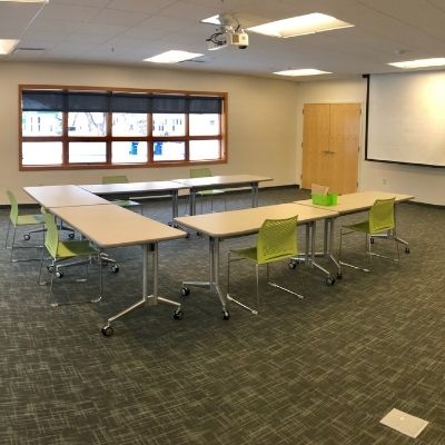 RCU Community Room. Large meeting room with window showing tables and chairs with a projector and retractable screen.