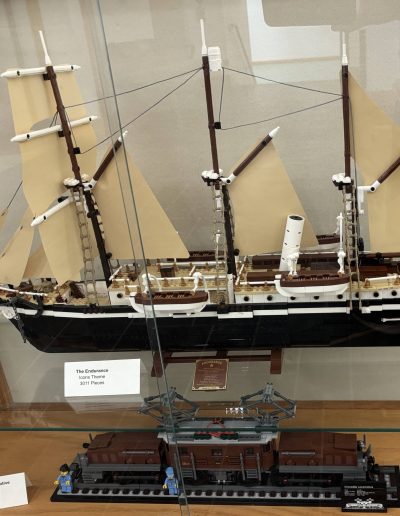 LEGO ship and train models displayed in a wooden glass case, with labels detailing the models.