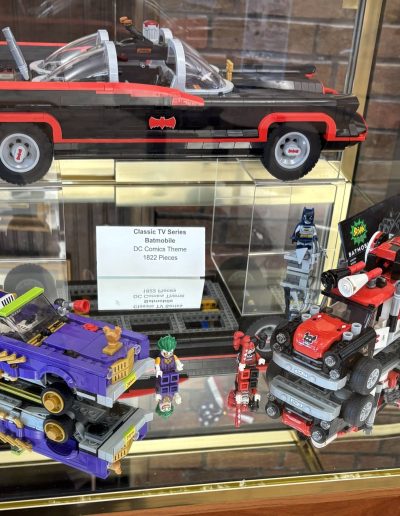 LEGO models of the Batmobile, Joker Lowrider, and Harley Quinn Cannonball in a display case.